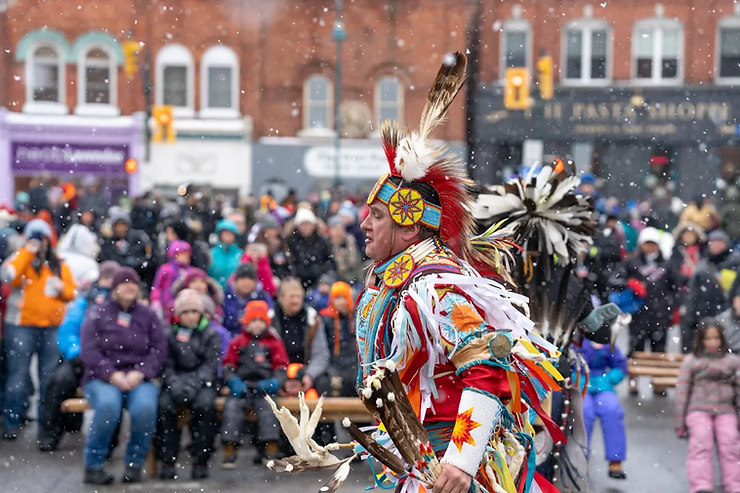 Fire and Ice Festival in Bracebridge, Ontario: downtown buildings, a crowd of residents watching performances from the street, an aboriginal dancer in traditional clothing with fire accessories.